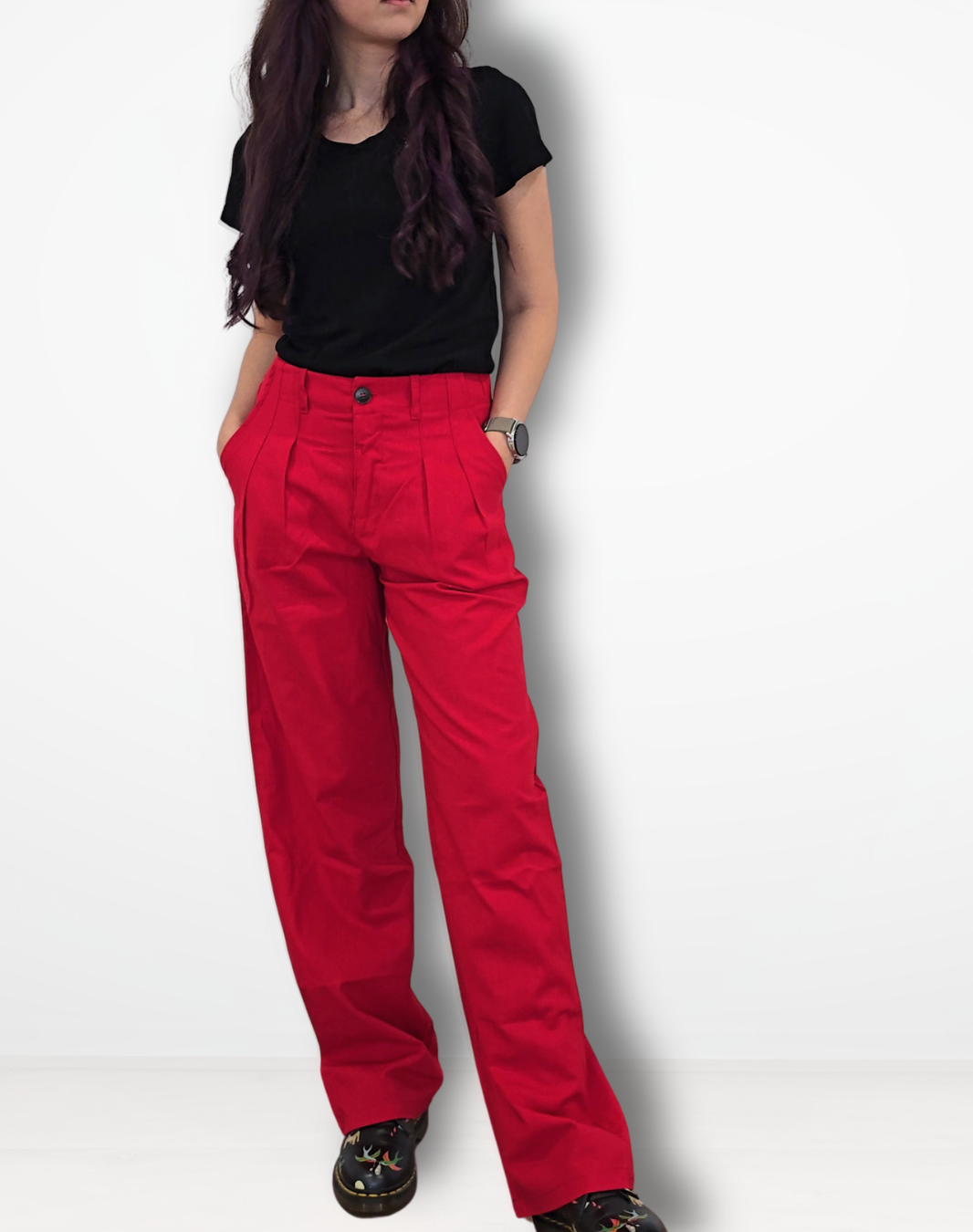 A woman modeling a pair of bright red wide-leg trousers with a black t-shirt and black shoes, standing against a white studio background.