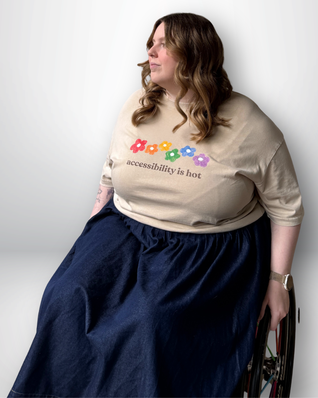 Person in a beige tee with a colorful logo and text, sitting in a wheelchair on a white background