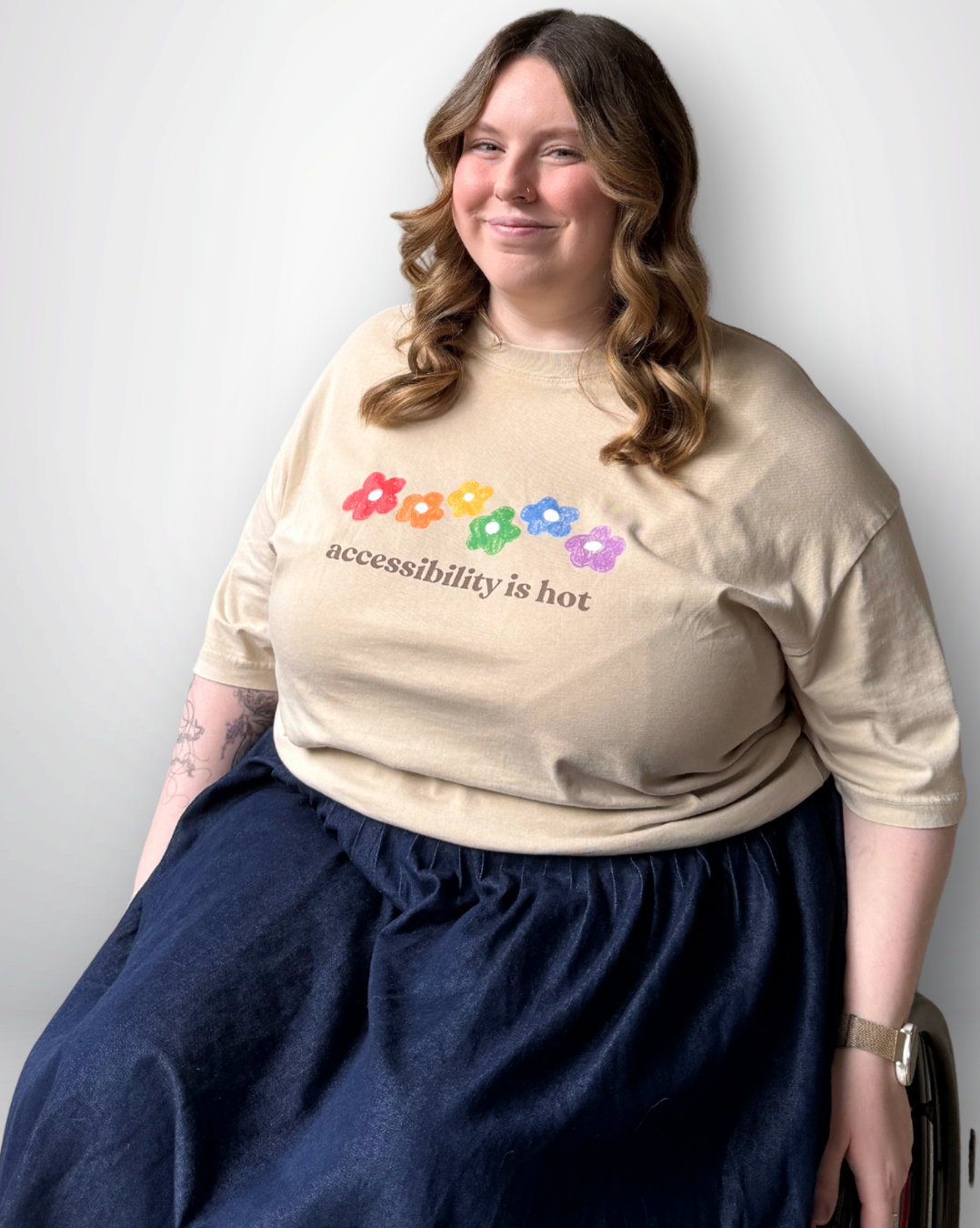 Person wearing a beige tee with colorful graphics and a blue skirt against a white background