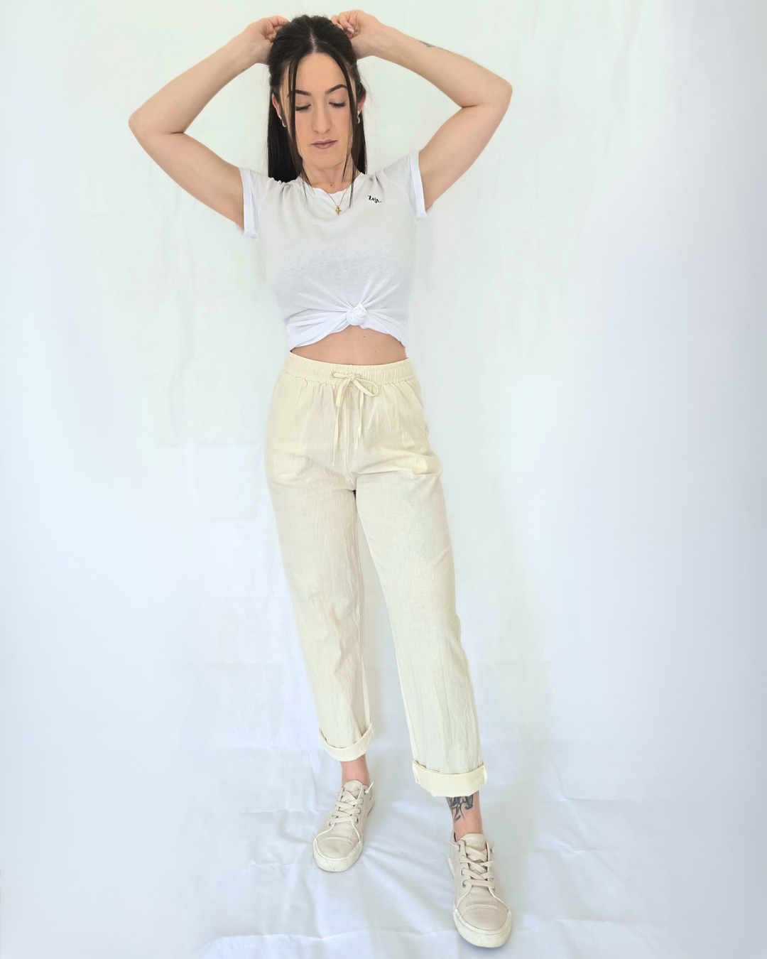 Person wearing a white tank top and light yellow pants on a white background