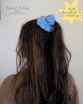 Person with a blue scrunchie in their hair, with text indicating 'Pastel Polka XXL Scrunchie' and '50% donated to charity'.