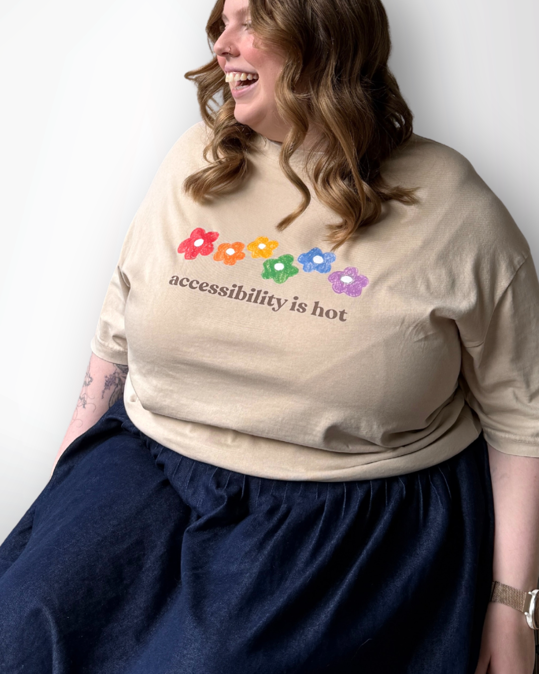 Person wearing a beige sweatshirt with colorful text and flowers, sitting against a white background