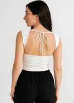 Woman wearing a white sleeveless top with open back and black pants on a plain background