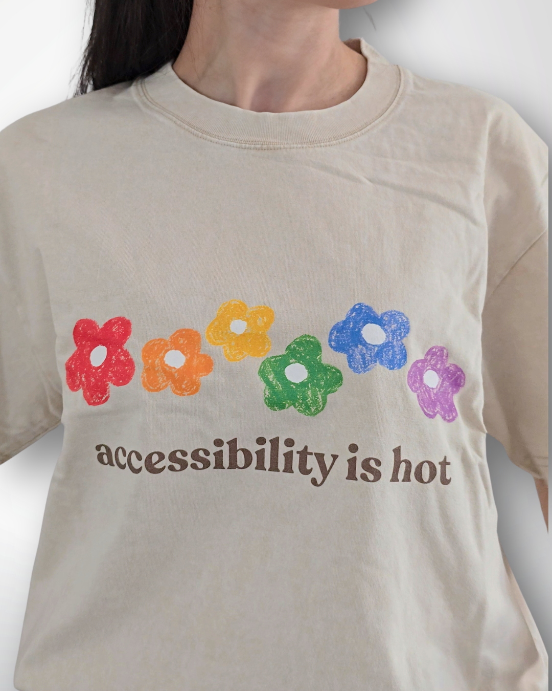 Beige t-shirt with colorful flowers and 'accessibility is hot' text on a plain background