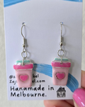 Pink coffee cup earrings on a 'Zejt' branded card held by a hand.