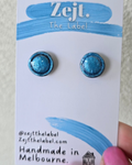 Blue glittery earrings on a 'Zejt' branded card held by a hand against a white background