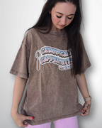 Person wearing a brown oversized t-shirt with graphic design on a plain background