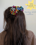 Person wearing a colorful scrunchie with text indicating charity donation and product name.
