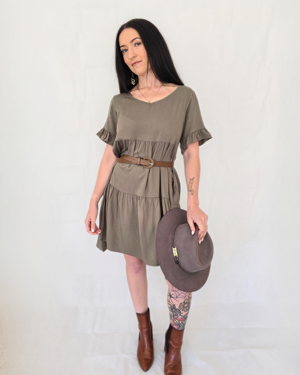 Woman wearing an olive green dress with a brown hat on a white background