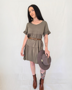 Woman wearing an olive green dress with a brown hat on a white background