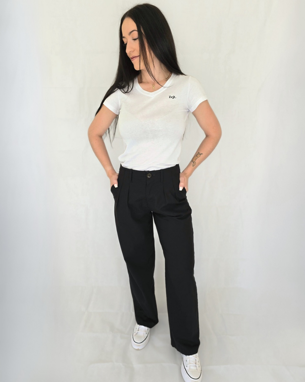 Woman wearing a white t-shirt and black pants against a plain background