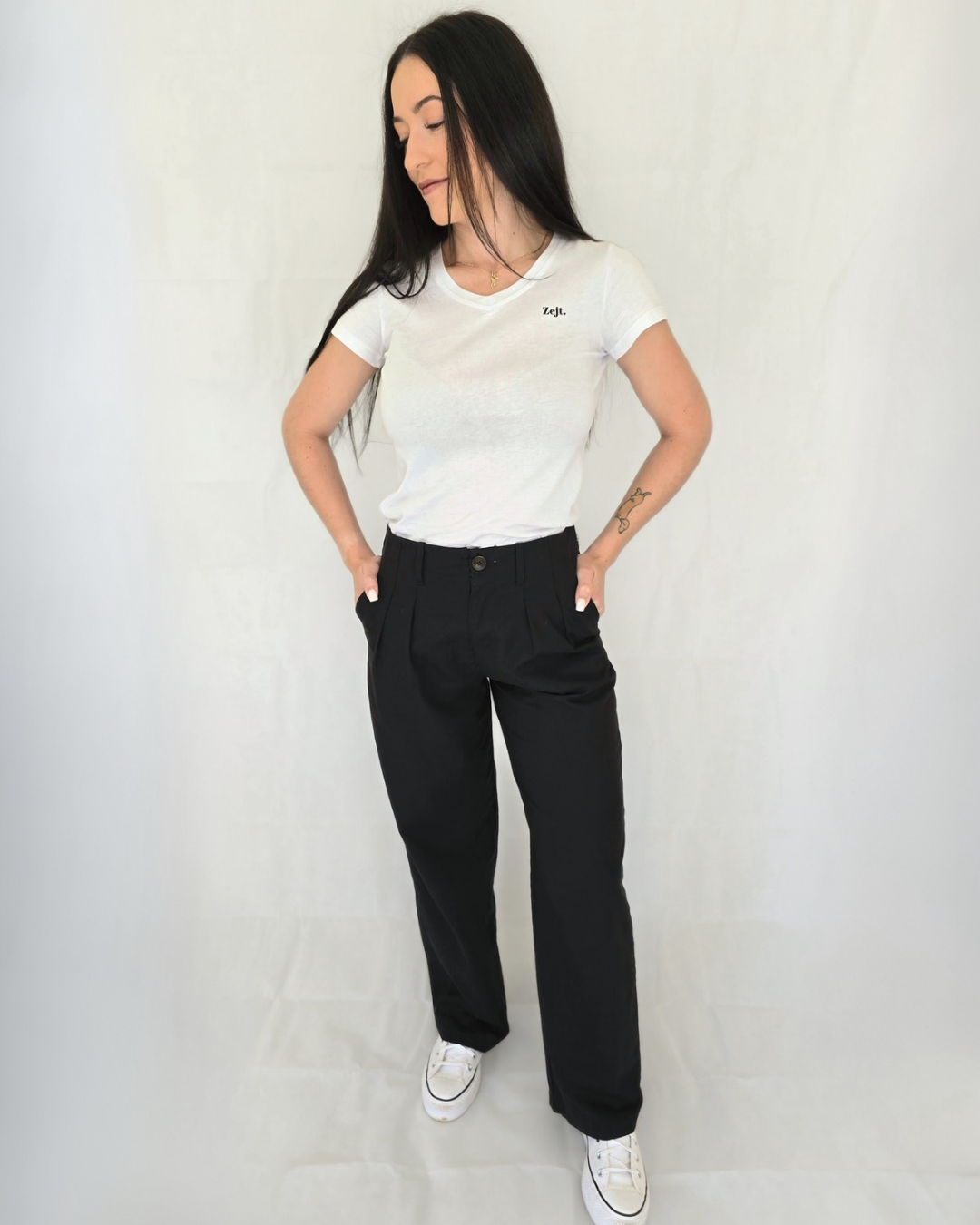 Woman wearing a white t-shirt and black pants against a plain background