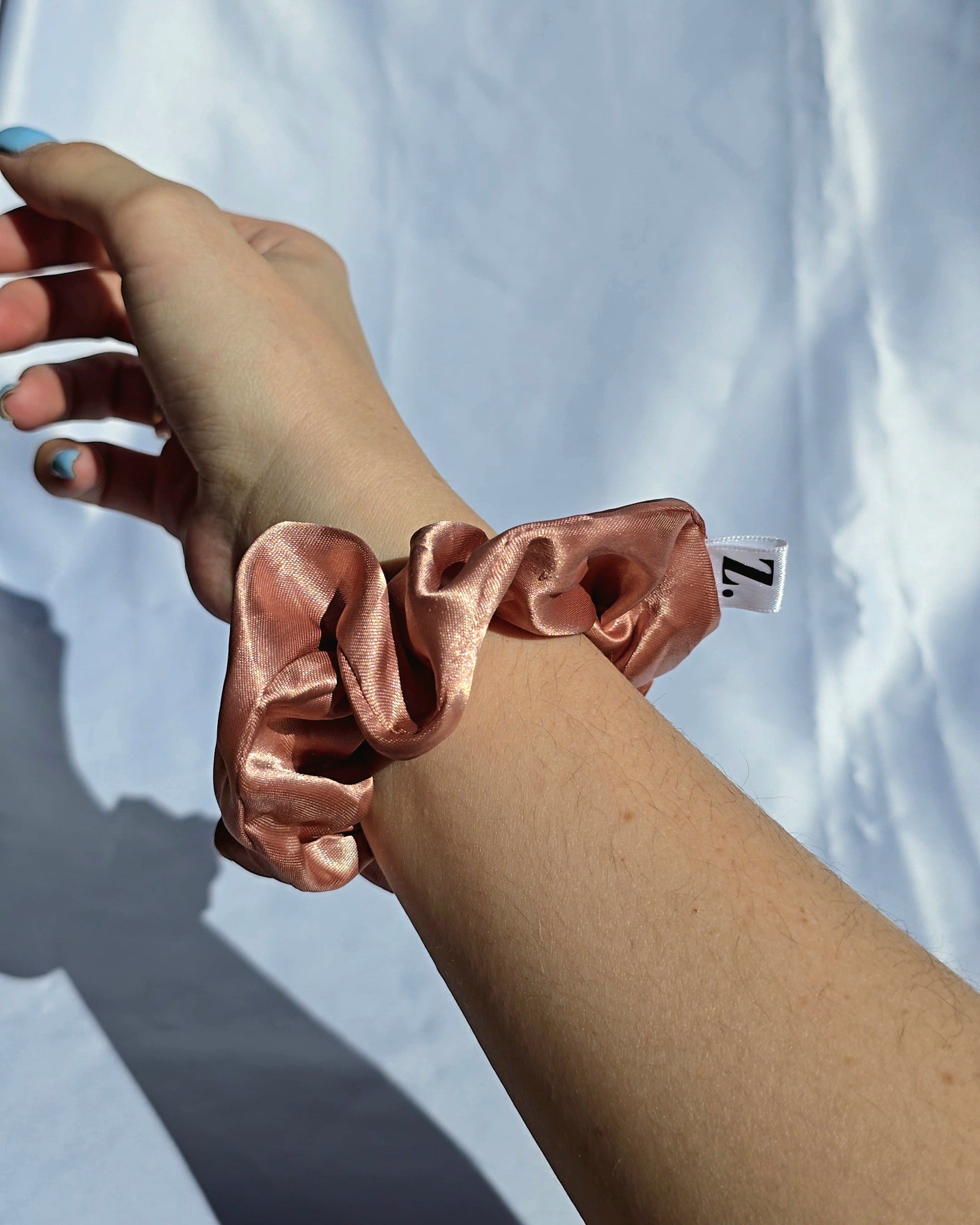Rose gold scrunchie on a wrist against a light blue background