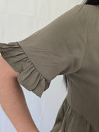 Close-up of a person wearing a green dress with ruffled sleeves against a white background rayon fabric detail