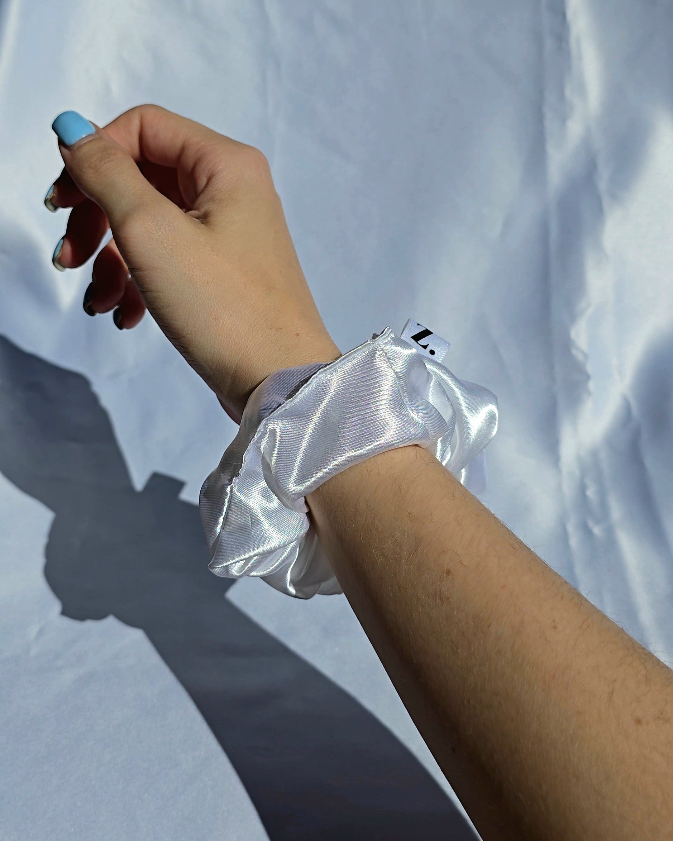 Hand wearing a white satin scrunchie in the sun